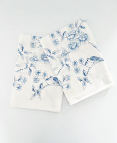 two napkins with blue and white flowers on them sitting next to each other in front of a white background