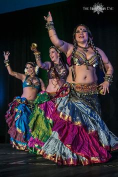 belly dancers performing on stage in colorful outfits and headdress, with their arms raised