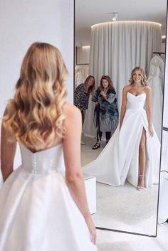 a woman in a wedding dress looking at herself in the mirror