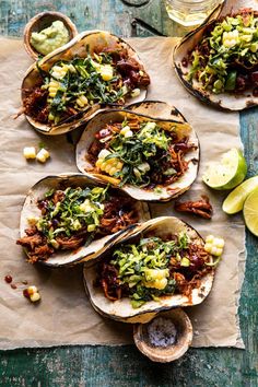 several tacos with various toppings on top of paper next to lime wedges