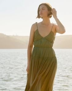 a woman in a green dress is standing by the water and looking off into the distance