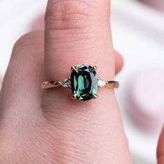 a close up of a person's hand with a green ring on their finger