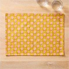 a place mat with yellow and pink designs on it, next to two empty glasses