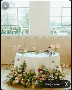 a table with flowers and greenery on it in front of a window at a wedding reception