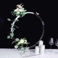 a table topped with white flowers and greenery next to two wine glasses on top of a table