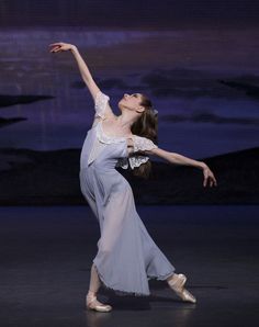 a woman in a gray dress is dancing on the dance floor with her arms outstretched