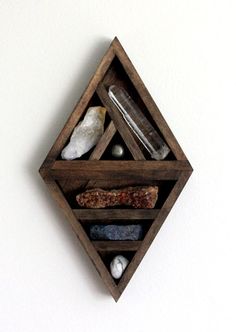 a wooden shelf with rocks and other items in it on a white wall behind the shelves