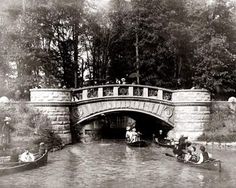 an old black and white photo of people on boats under a bridge