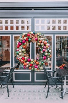 a christmas wreath on the front door of a store with two chairs and tables outside