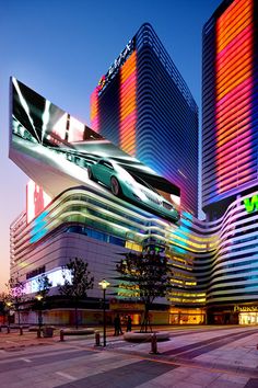 the modern building is lit up with colorful lights and has cars parked in front of it