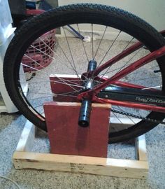 a red bicycle is being worked on by someone using a small wooden stand to hold the spokes