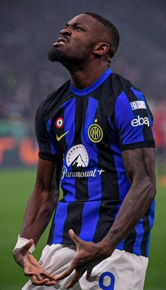 a man standing on top of a soccer field wearing a blue and black striped shirt