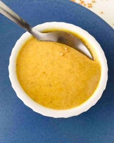 a bowl of soup with a spoon in it sitting on a blue plate next to an orange and white napkin