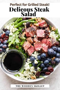 a white bowl filled with blueberries, meat and salad next to a small jar of dressing