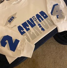 a white shirt with blue letters and arrows on the front is sitting on top of a carpeted floor