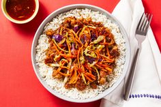 a bowl filled with rice, meat and veggies on top of a red table