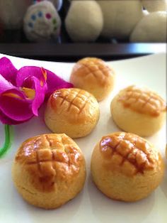 several small pastries on a white plate next to a pink flower