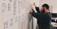 a man standing next to a whiteboard covered in notes and writing something on it