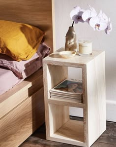 a small wooden table with a vase on it next to a book shelf and bed