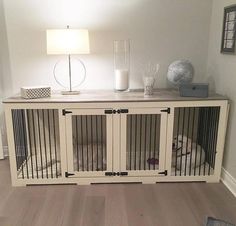 a dog is laying in its cage on the floor next to a table with a lamp