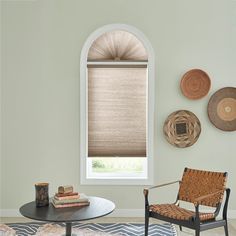 a living room with two chairs and a table in front of a window that has roman shades on it