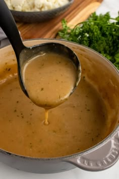 a ladle full of gravy being poured into a pot