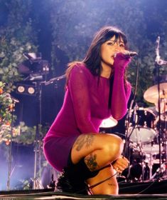 a woman kneeling down on top of a stage next to a microphone and drum set