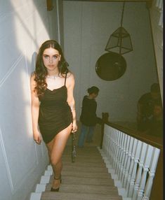 a woman in a black dress is walking down the stairs