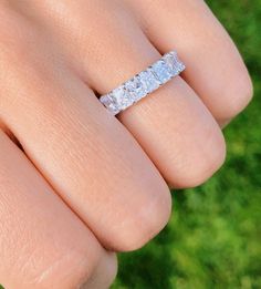 a woman's hand with a wedding ring on it, in front of green grass