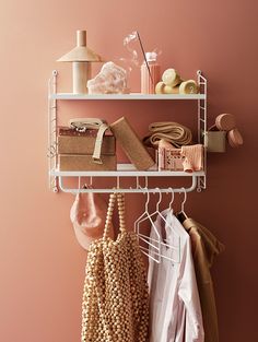 a white shelf filled with lots of clothes and other items next to a pink wall