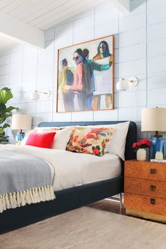 a bed sitting in a bedroom next to a painting on the wall