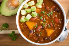 a bowl of chili and avocado soup on a cutting board