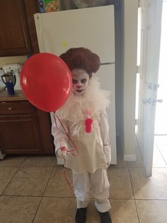 a clown holding a red balloon in front of a white refrigerator with brown cabinets and tile flooring