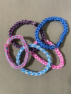 four different colored braided bracelets sitting on top of a gray surface with one knot in the middle