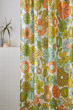 an orange and green floral shower curtain hanging on a bathroom wall next to a potted plant