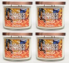 four candles with labels on them sitting in front of each other and one candle is filled with autumn leaves