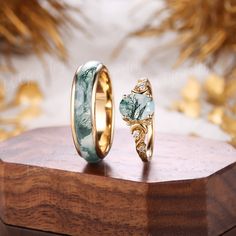 two wedding rings sitting on top of a wooden stand next to each other with gold leaves