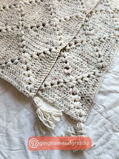 a crocheted blanket laying on top of a bed with tasseled edges