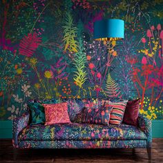 a couch with colorful pillows on it in front of a floral wallpaper