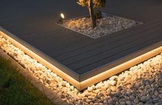 a lit up deck with rocks and plants in the foreground, next to a small tree