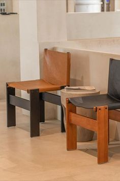 two wooden chairs sitting next to each other on top of a tile floor in front of a white wall