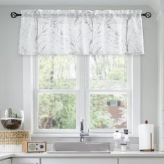 a kitchen window with white curtains and dishes on the windowsill, next to a sink