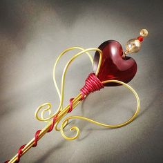 a red and gold heart shaped object on a white surface with a cord attached to it