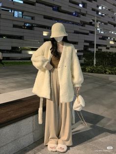 a woman wearing a white fur coat and wide brimmed hat is standing in front of a building