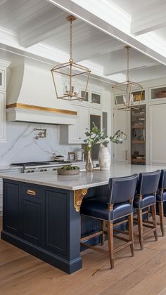 a large kitchen island with blue chairs and gold trim on the countertop is surrounded by white cabinets