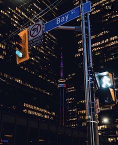 a street sign and traffic light in front of some tall buildings at night with lights on