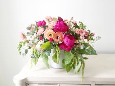 a white vase filled with lots of pink and red flowers on top of a table