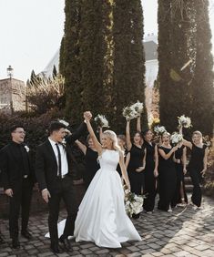 the bride and groom are holding their arms in the air as they walk down the street