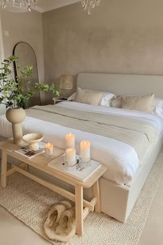 a white bed sitting next to a table with candles on top of it in a bedroom