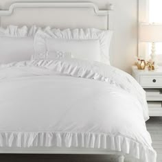 a white bed with ruffled sheets and pillows